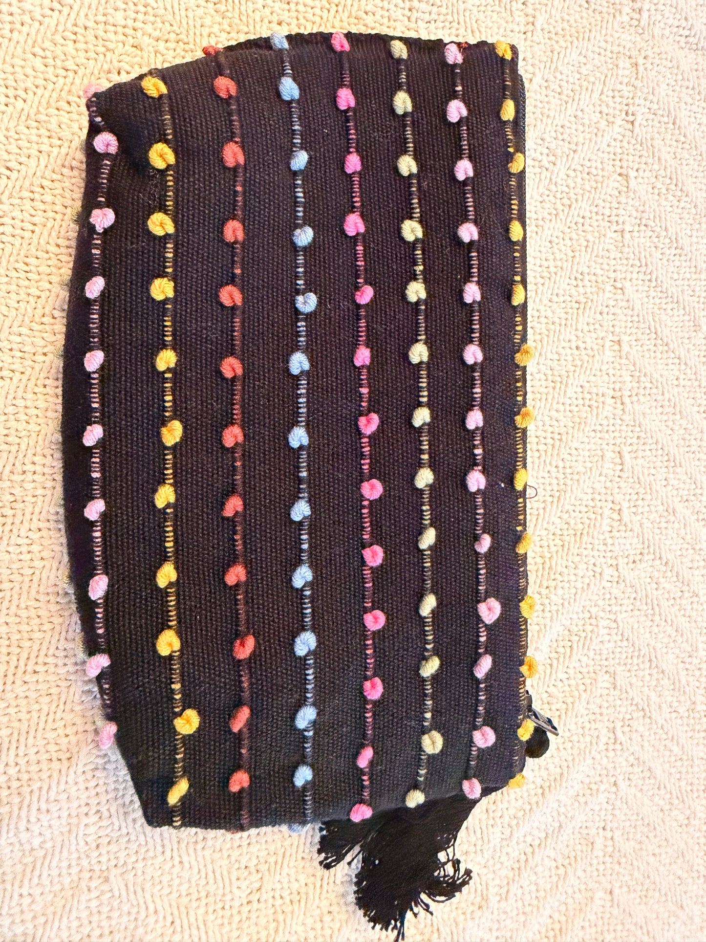 Black pouch with colorful pom-pom details on a beige surface